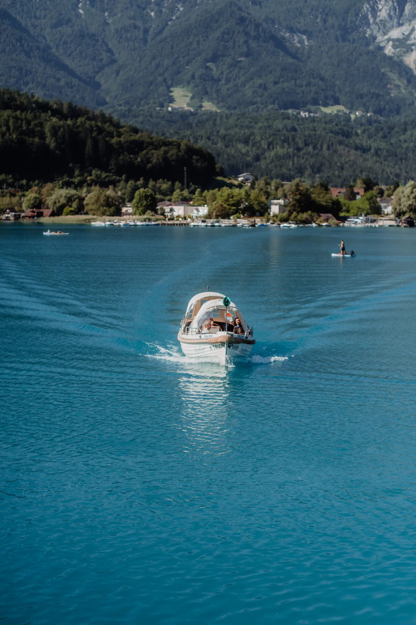 Das Boot „Falke" auf der Überfahrt: türkises Wasser, dahinter das Ufer und die Karawanken.