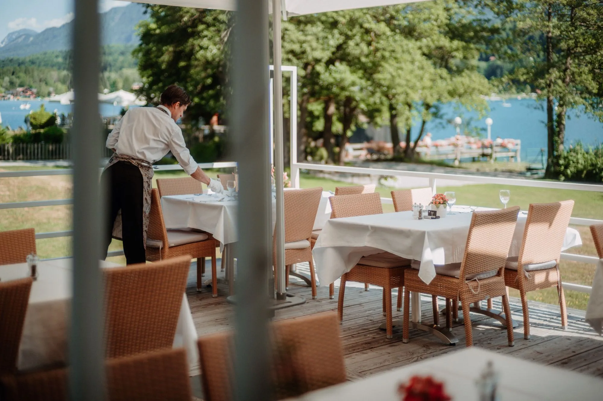 Die Terrasse über dem See: gedeckte Tische, ein Kellner, dahinter das Wasser.