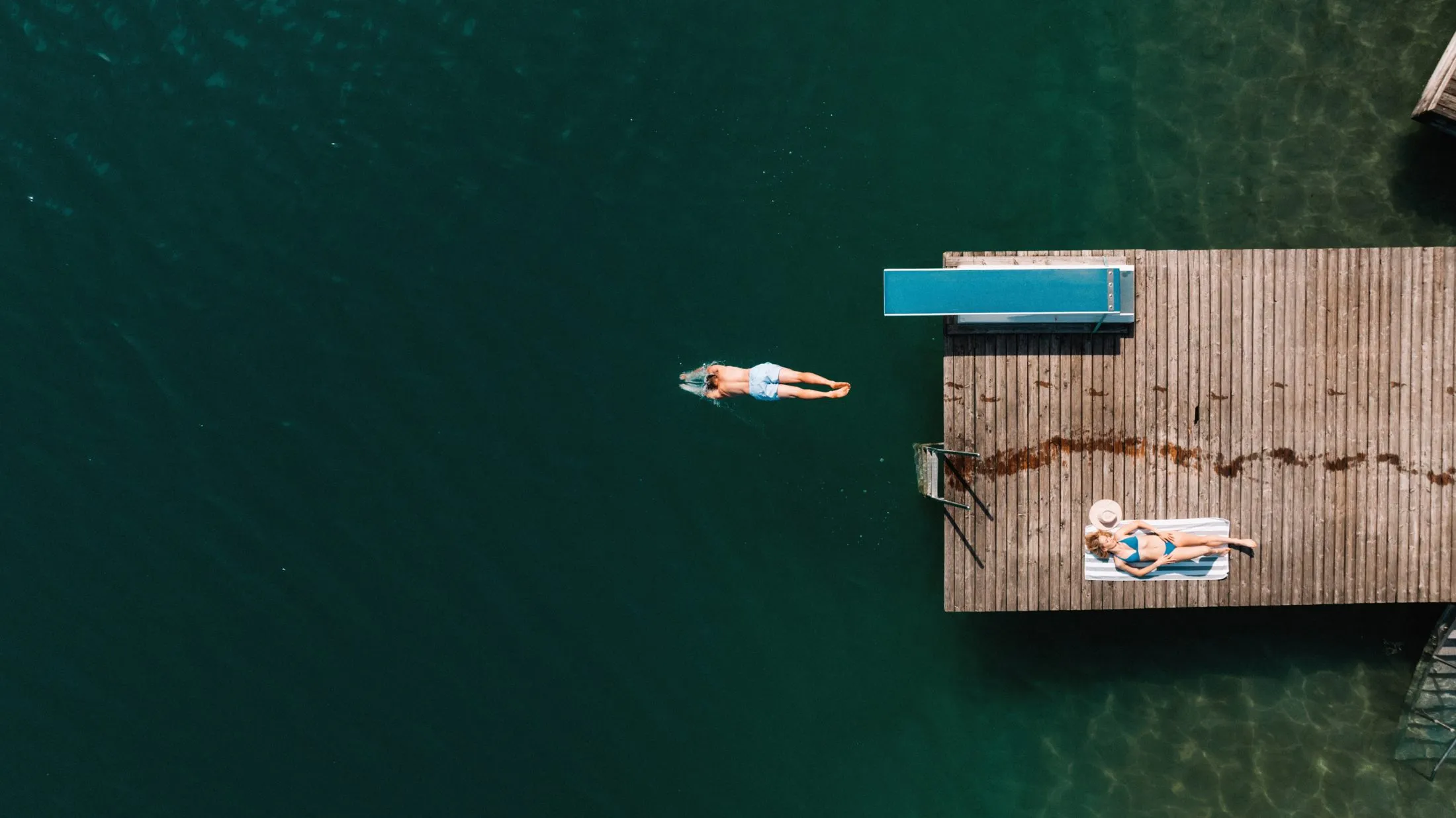 Der Badesteg senkrecht von oben, daneben eine Schwimmerin im klaren Wasser.